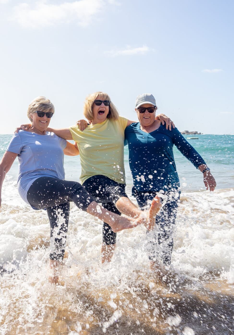 Lovely group of senior girl friends on their 60s walking and having fun splashing water on sea. Three mature healthy retired females Laughing and enjoying retirement and outdoors active lifestyle.